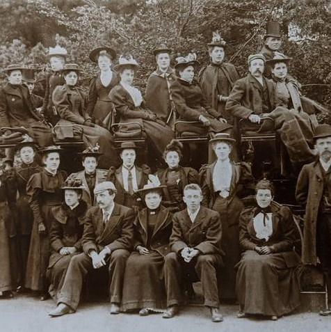 A staff outing of Beales staff in the late 19th century with about 25 men and women seated on and around a vintage vehicle