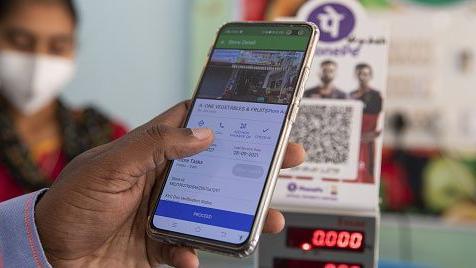 The picture shows the hand of a man using his mobile phone to scan a QR code and make a digital payment. 
