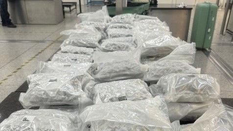 Lots of vacuum sealed white plastic bags laid out on a table. Two green suitcases are in the background in an airport hall.
