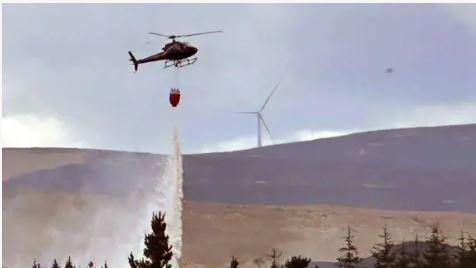 Heileacoptair a' dòrtadh uisge air teine monaidh