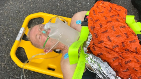 Graham Sharpe on a yellow stretcher on the road. He is surrounded by medical equipment.