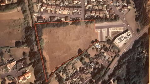 A close up of an aerial map showing residential houses surrounding a large patch of brown land. The land has been outlined with a red line, to show where the development would be.