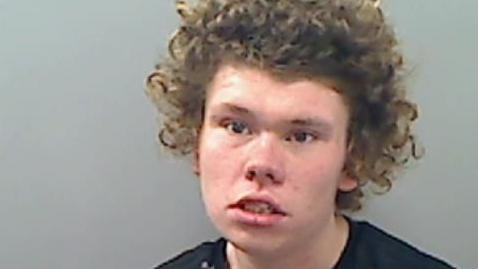 Mugshot of Thomas Rogers, he has curly brown hair and is wearing a black t-shirt