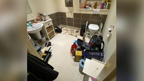 A bathroom with a number of items on the floor, including blue roll, a dust sheet, a backpack and some tools.