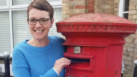 A smiling Dinah Johnson posing as she puts a letter into a postbox