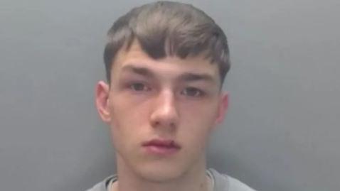 A mugshot of Jack Lawson. He has brown hair and a split upper lip. He is wearing a grey jumper.