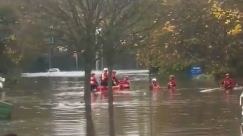 A picture of people in red jackets and helmets in red boats on brown water with trees sticking up through it