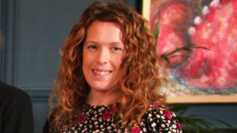 A smiling Laura Sweetenham. She has long, fair, wavy hair and is wearing a black, white and red patterned dress.