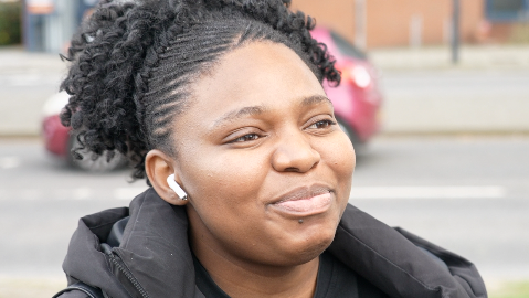A lady in a black puffa style coat with airpods in her ear. 