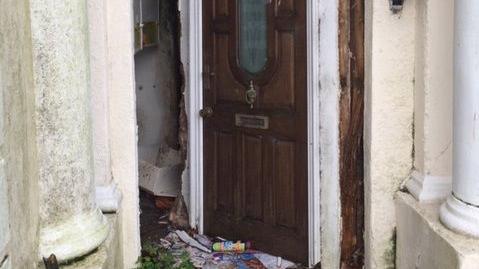 An old property with an ajar door and rubbish by the threshold.