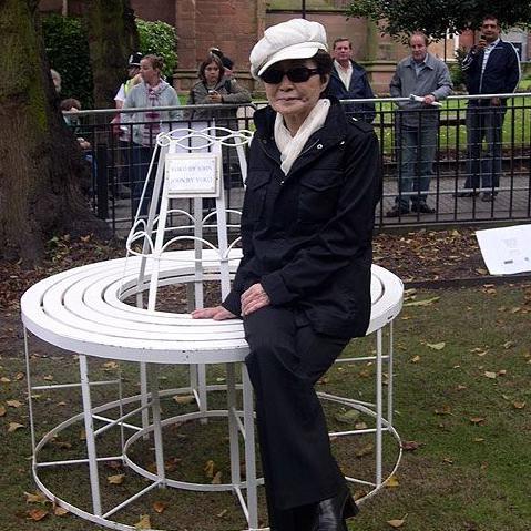 Yoko Ono pictured sitting on a replica of the original bench she and John Lennon had brought to the city in 1968