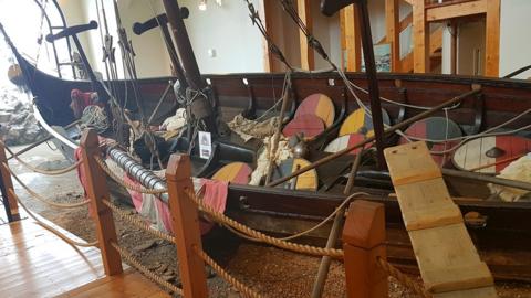 An exhibition of a small Viking longboat being cleaned by a model of a Viking man.