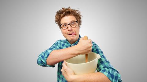 A man sticks his tongue out as he mixes ingredients in a bowl.