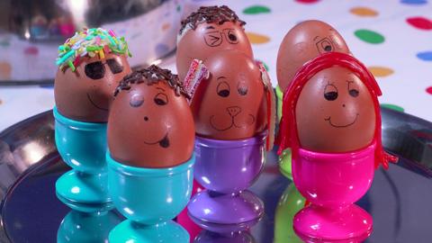 Six eggs, with faces drawn on, and sprinkles and strawberry laces used for hair.