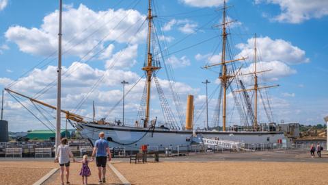 young-girl-walks-toward-large-ship-holding-hands-with-two-adults.