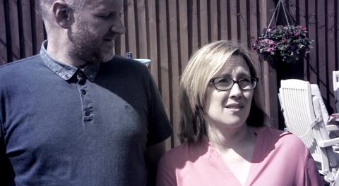 Woman looks uneasy stood next to husband, looking at something out of shot.