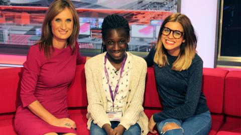A girl sits with two women on the BBC News sofa.
