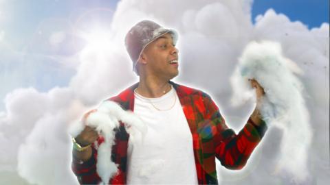 A young man in a bucket hat is holding big pieces of cotton wool, behind him is a sky background