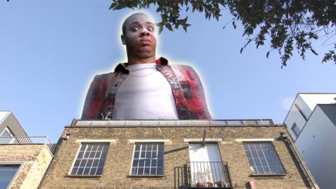 A giant young man is crashing through the top of a large building