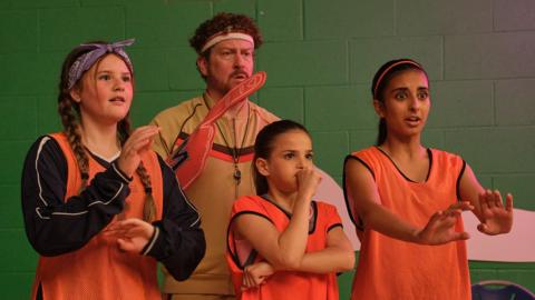 A team of basketball players and their coach watch a basketball game excitedly and nervously