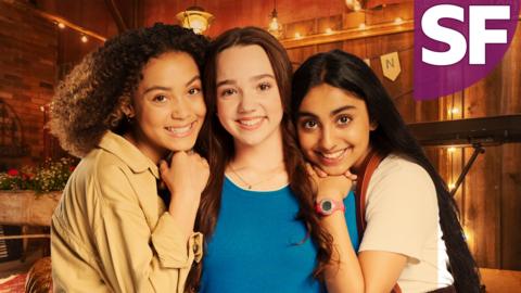 Three girls are looking to camera smiling, the middle girl has the other two girls leaning on either side of her.