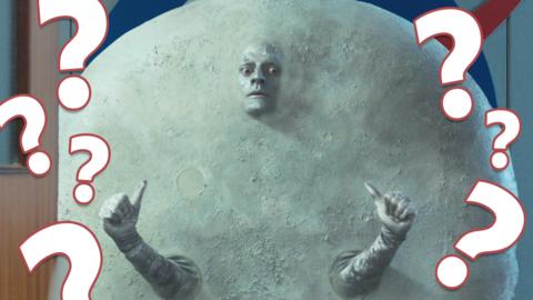 Image of a man dressed like the moon with question marks on his left and right.