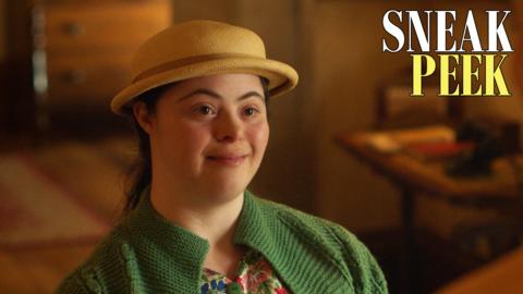 Nancy, a young girl in a green cardigan and a hat, she is smiling.