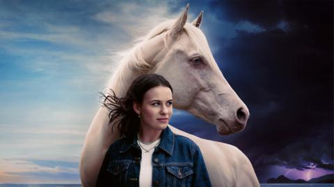 Image of a girl with a large white horse, Issie from Mystic, she is looking out over a beach.