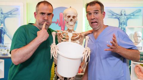 Dr Chris and Dr Xand pose with a skeleton and a bucket.