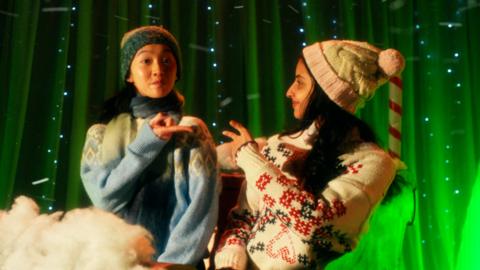 Two girls are dancing on a sleigh surrounded by green lights