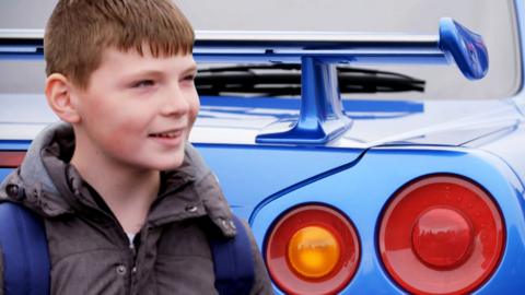 A boy in front of a car spoiler.