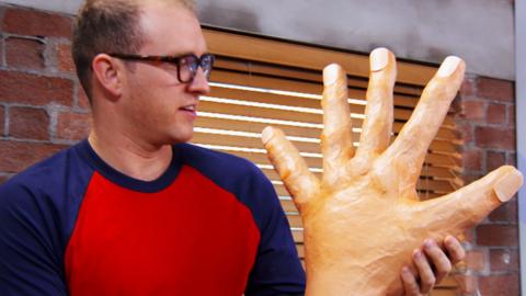 A man holing a big paper mache hand.