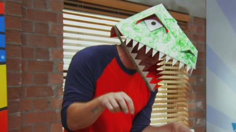 A man (Ricky Martin) wearing a dinosaur mask.