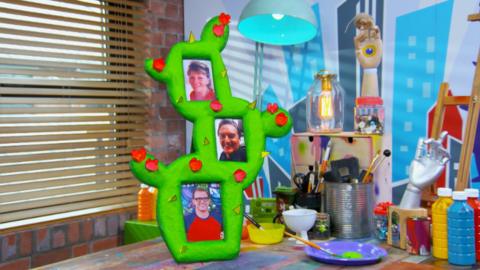 Handmade green cactus photo frame standing on a colourful art desk.