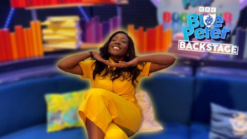 Blue Peter's Mwaksy sits on the Blue Peter sofa with her hands under her chin smiling.