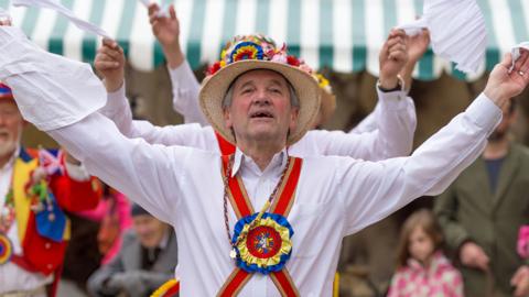 A morris dancer wearing a straw hat and bright colours.