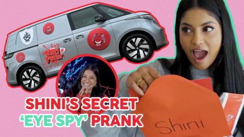 Shini opens a mystery red envelope with a surprised look on her face.