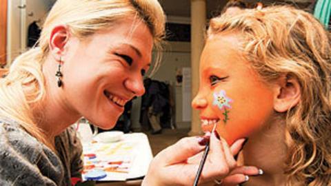 A girl having her face painted by a woman