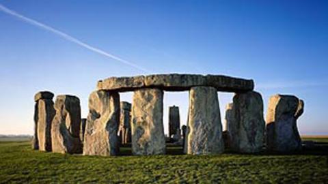 A wide view of Stonehenge with a bright blue sky in the background.