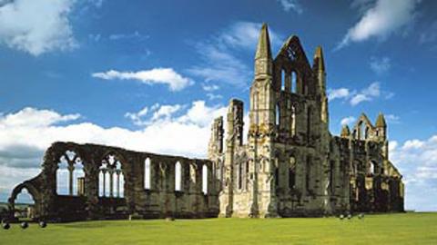A larged, ruined abbey. With a blue sky and green grass