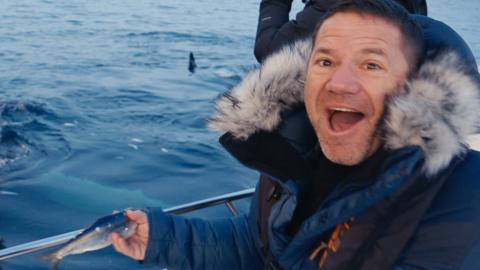 Steve Backshall holding a fish looking shocked.