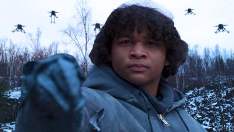 Johnny holds up his blaster as he's surrounded by robot drones in the sky.