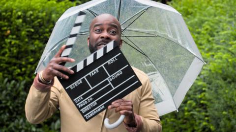 Melvin Odoom holding a clapper board.