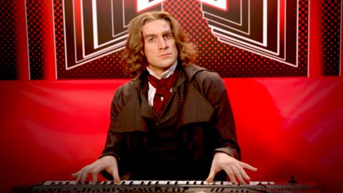 A man dressed as Ludwig van Beethoven playing an electric piano.