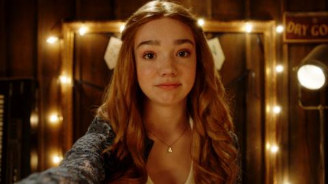 Holly Hobbie is looking into the camera, smiling. There are fairy lights behind her.