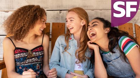 Three girls are sitting on a bench smiling and laughing.