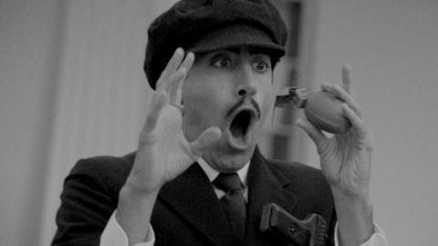 A man with a mustache looking shocked with a grenade.