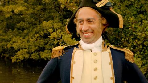 A man dressed as navigator James Cook wears a slightly strained smile.