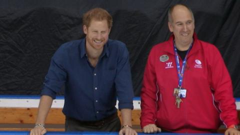 Prince Harry smiles as he watches skaters on the ice, next to one of the Nottingham Ice Arena coaches.