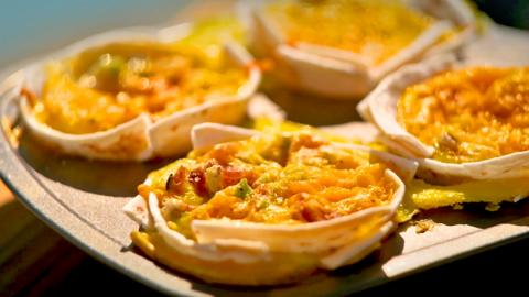Two tortilla cups resting on a wooden board with four in a tray behind.
